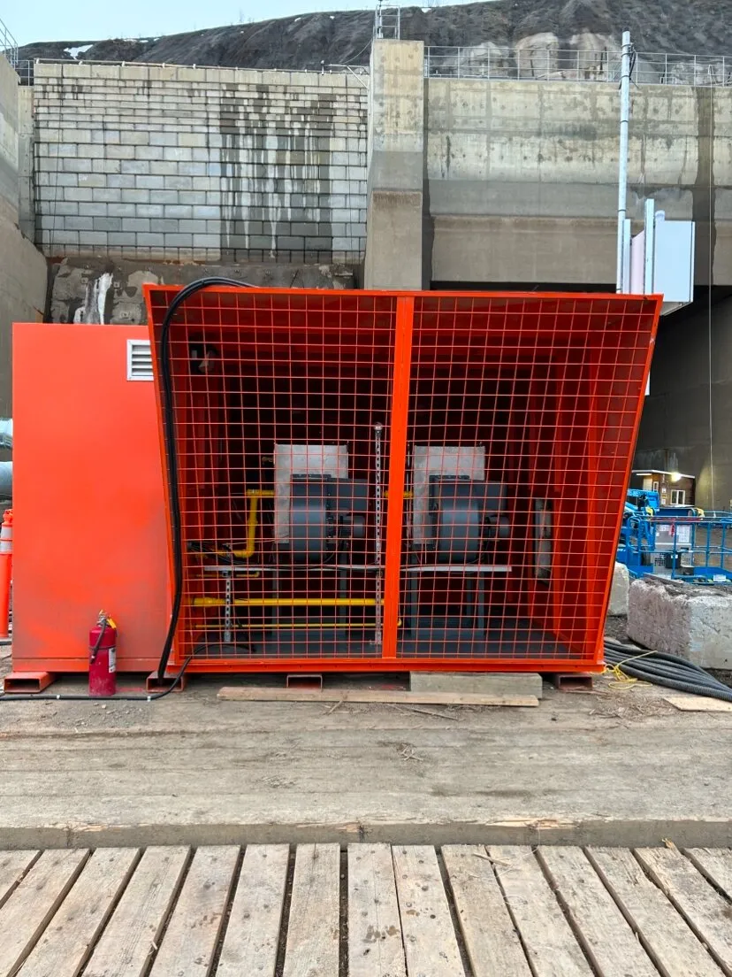 Caged mine air heater installed on a timber deck beside a concrete retaining wall