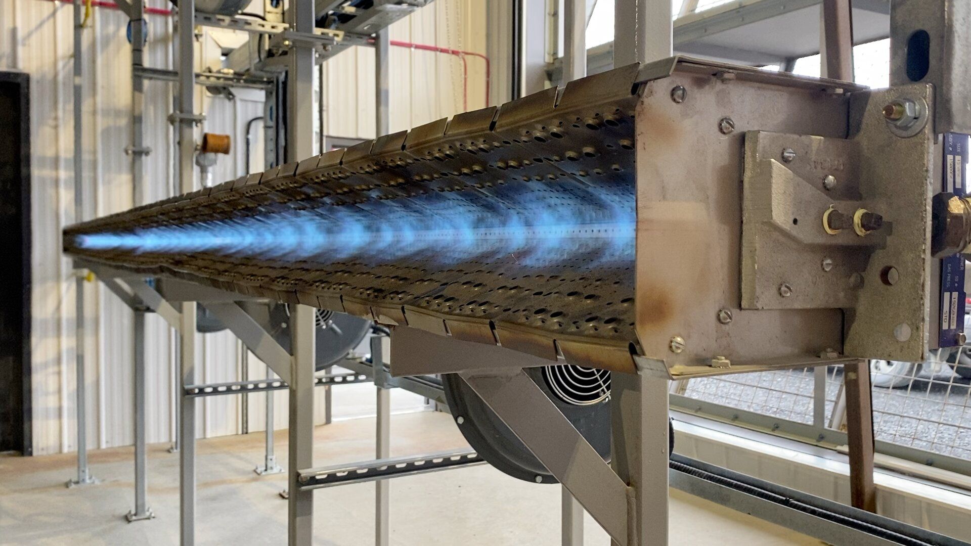 A direct-fired line burner running on the test stand at the BCE Combustion shop, flame carried the full length of the manifold